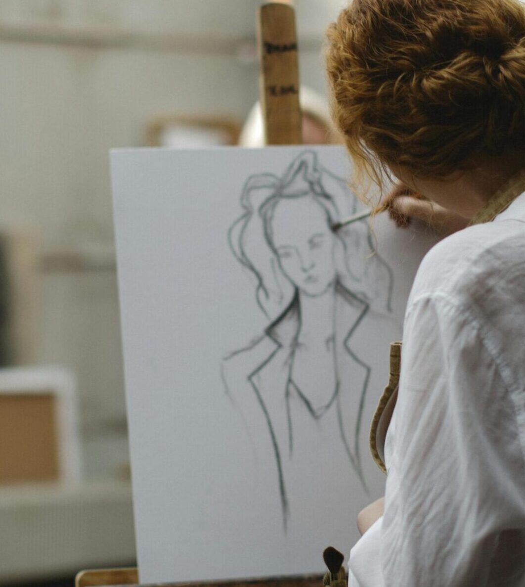 A young woman focuses intently as she sketches on an easel in an art studio.